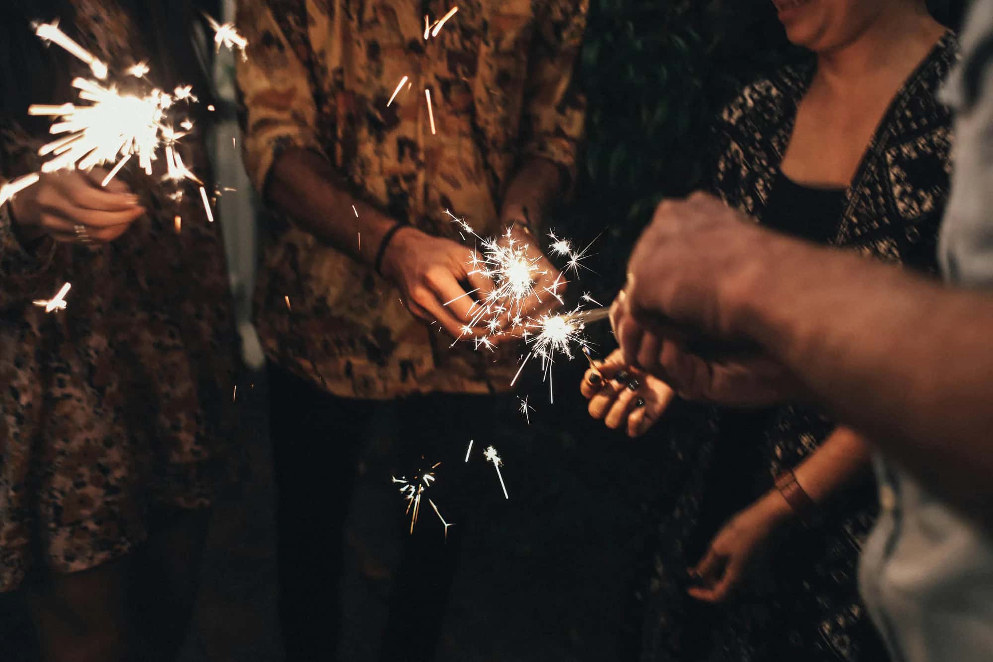 Guests holding lit sparklers close together at a night gathering